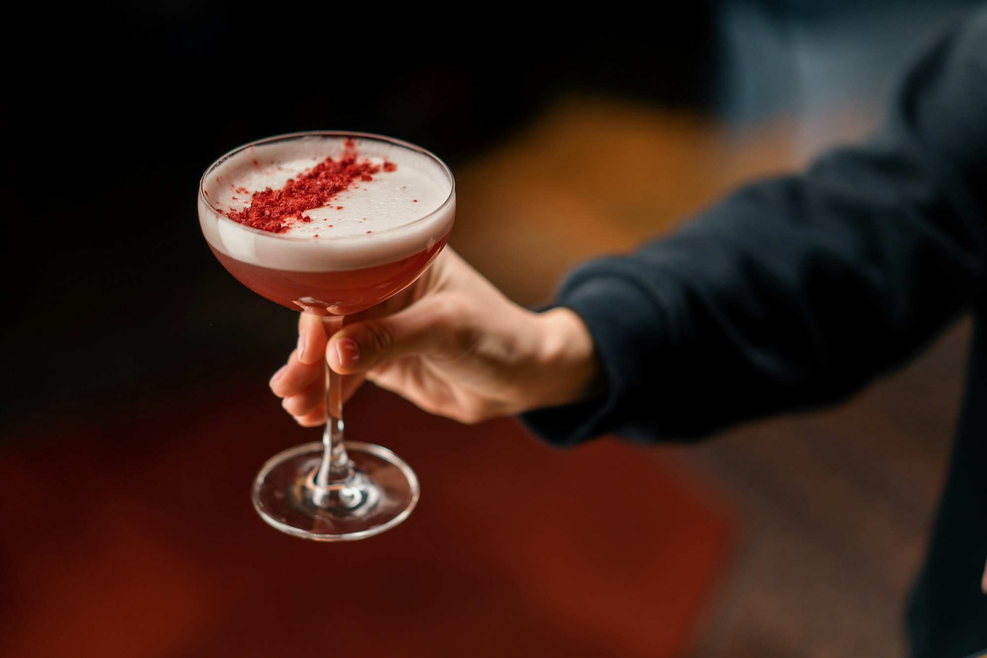 customer holding delicious pink freshly made raspberry milk punch cocktail in hand bar