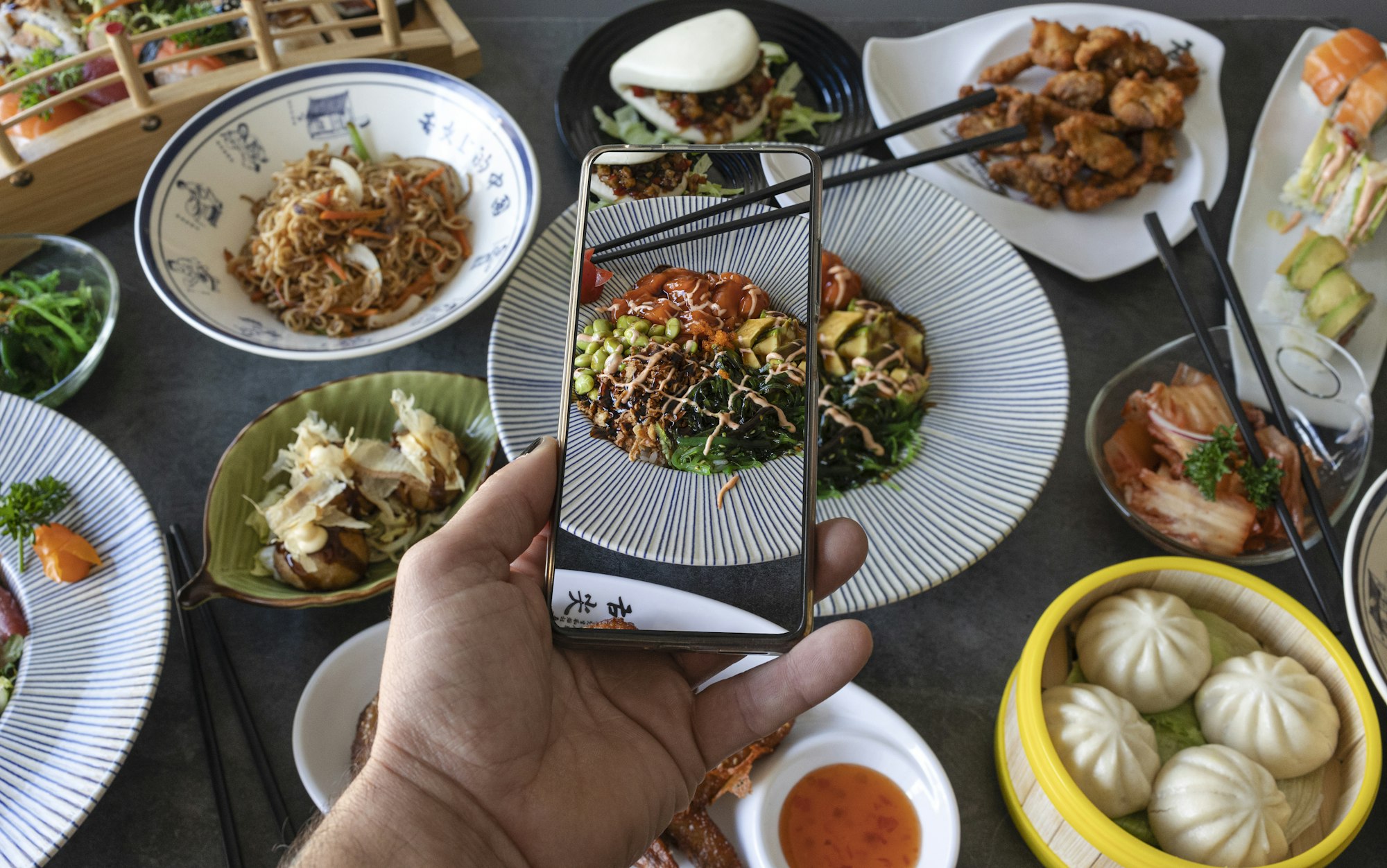 Man taking photos of Japanese food at restaurant table.